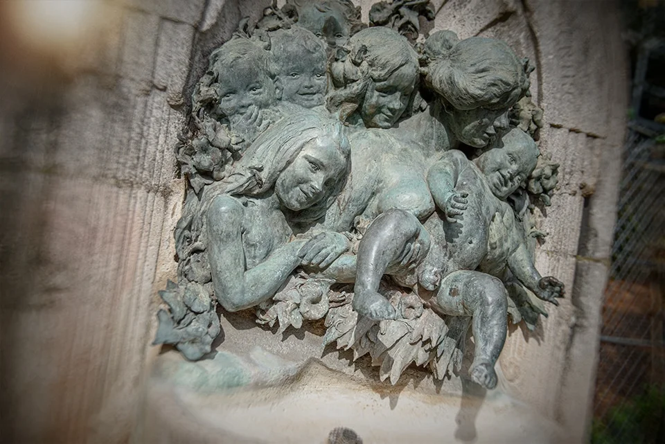 Sculpture en haut relief d'une fontaine montrant des femmes tenant un bébé en train de faire pipi.