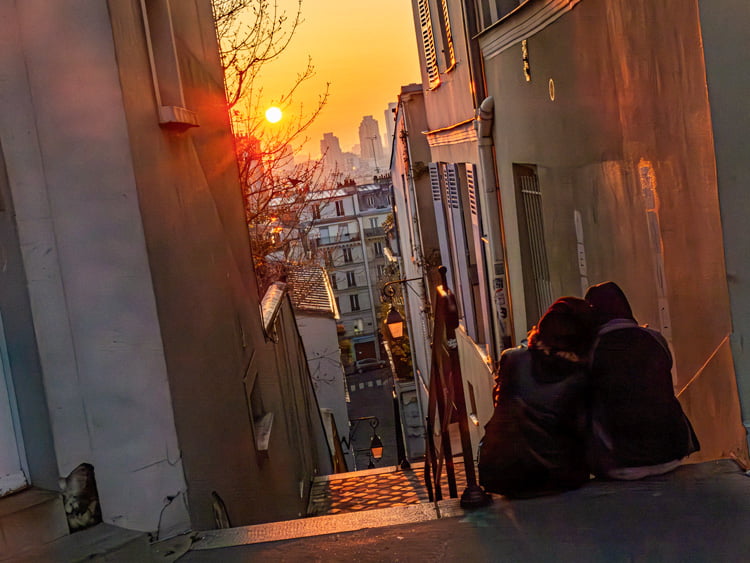Au sommet d'un escalier de Montmartre, deux personnes assises regarde le levé de soleil flamboyant.