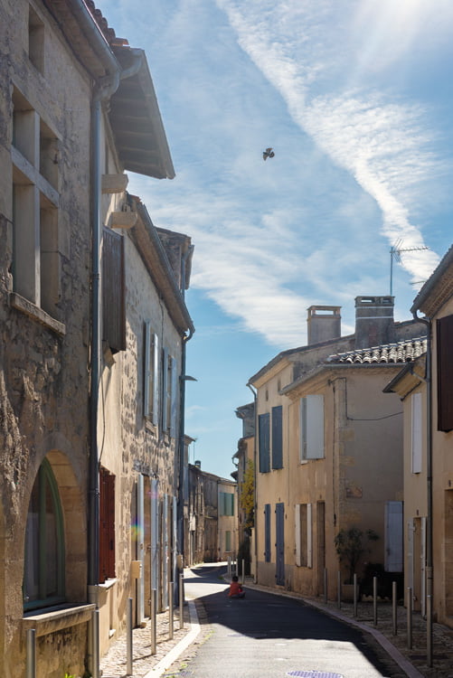un enfant assis devant son ballon rouge dans une ruelle du sud de la france et dans le ciel, un oiseau vole.