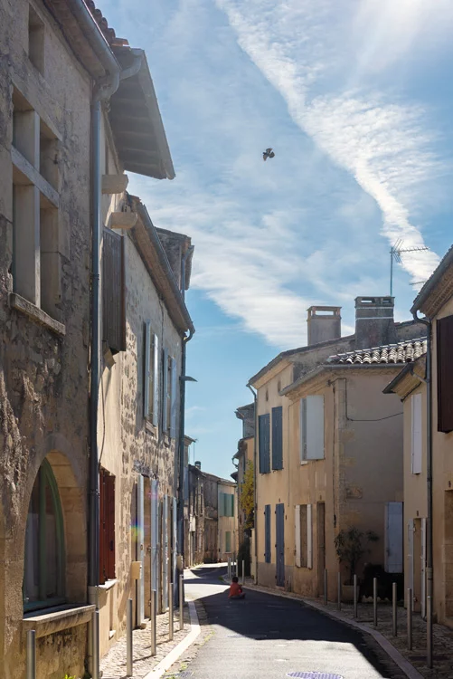 un enfant assis devant son ballon rouge dans une ruelle du sud de la france et dans le ciel, un oiseau vole.