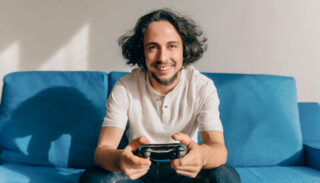 Un homme ressemblant à léonard de vinci joue avec une console de jeu vidéo assis sur un canapé