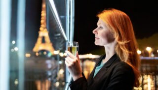 une jeune femme regarde dans une coupe de champagne le reflet de paris la nuit